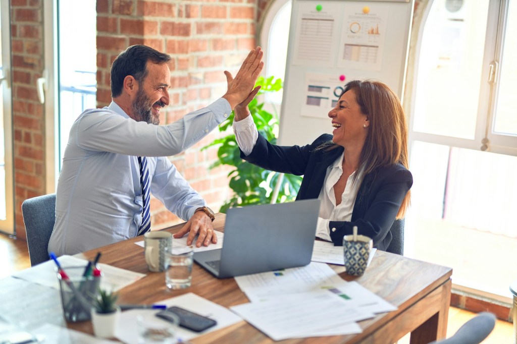 two business people high fiving at a table with a laptop between them